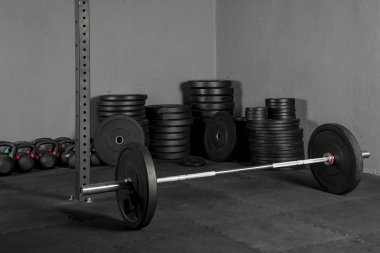 Barra de peso con discos para hacer ejercicio, y discos de varios pesos en el fondo