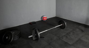 Barra de levantamientos con discos de varios pesos, pelota y cojin para ejercicios sobre piso de goma y save gris