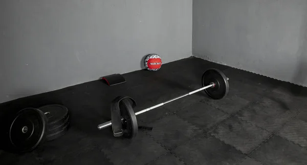 Barra de levantamientos con discos de varios pesos, pelota y cojin para ejercicios sobre piso de goma y save gris