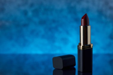 Mermer bir yüzey üzerinde yoğun şarap renkli ruj. Mavi arka plan ve soldaki yazı için boşluk.