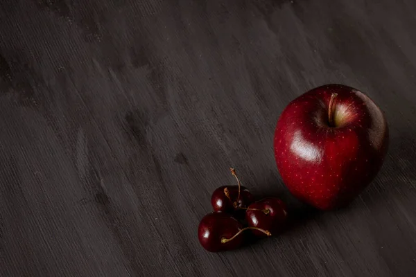 Apple accompanied by cherries on a vintage black table. With space for text
