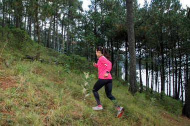 Ormanda koşan bir sporcu göle yakın bir dağa tırmanıyor.