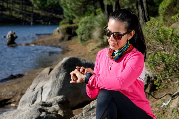 Koşucu kadın ormanda koştuktan sonra akıllı saatini kontrol ediyor.