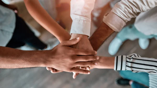 We zijn sterk. Bovenaanzicht van zakenmensen die elkaars hand bij elkaar houden terwijl ze op kantoor staan — Stockfoto