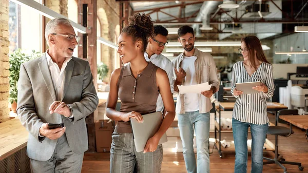 Voor de vergadering. Twee zakenexperts bespreken iets terwijl ze met collega 's door de kantoorgang lopen — Stockfoto