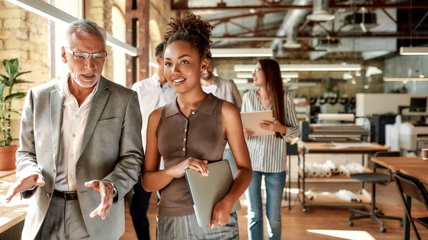 Condividere idee. Due esperti di affari discutono qualcosa mentre camminano con i colleghi attraverso l'ufficio corrido — Foto Stock