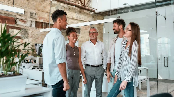 Feliz e bem sucedido. Grupo de empresários alegres de pé no escritório moderno, sorrindo e discutindo algo — Fotografia de Stock