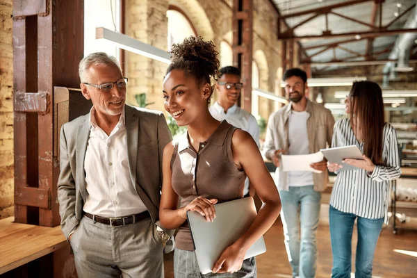 Compagni d'affari. Due colleghi discutono qualcosa e sorridono mentre attraversano il corridoio dell'ufficio — Foto Stock