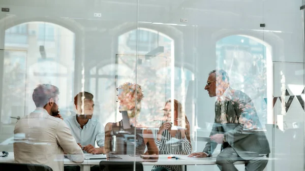 Office life. Group of business people discussing something while sitting at the office table behind the glass wall in the modern office