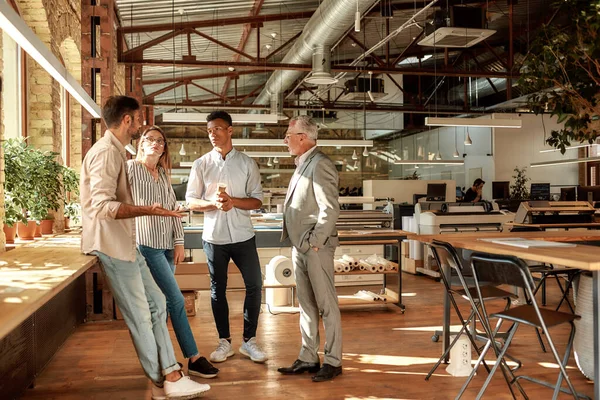 Snelle vergadering. Zakenmensen die koffiekopjes vasthouden en ergens over praten terwijl ze in het moderne kantoor staan — Stockfoto