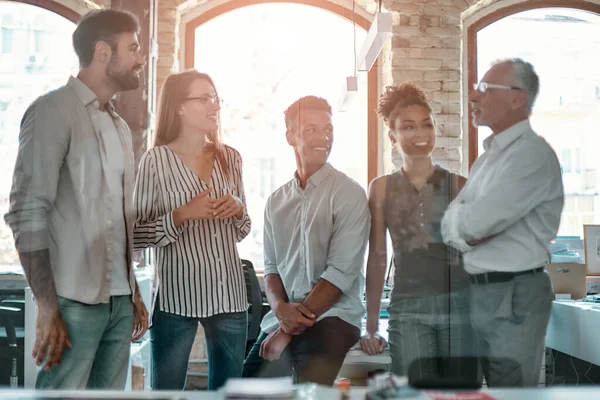 Pozitivní tým. Skupina veselých podnikatelů o něčem diskutuje a usmívá se, když stojí v moderní kanceláři — Stock fotografie