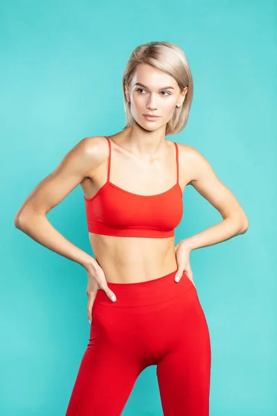 창녀같은 소녀. 빨간 운동복을 입은 젊고 섹시 한 금발의 여성 이 푸른 배경에 맞서서 바라보고 있습니다. 운동, 건강 — 스톡 사진