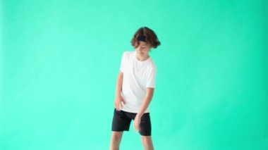 Genç basketbolcu. Spor giyim sektöründe genç bir çocuk yeşil arka planda dururken basketbol topuyla oynuyor.