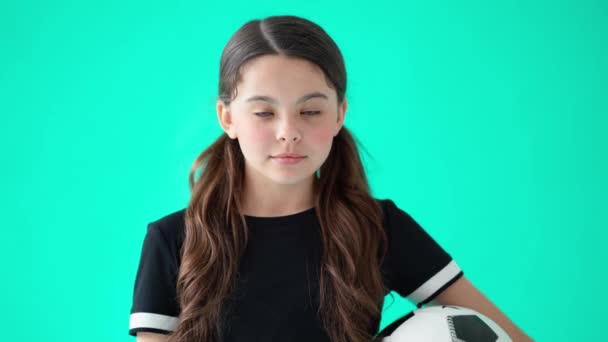 Head shot portrait of a cute teenage girl holding soccer ball, looking at camera and laughing, standing against turquoise blue background — Stock Video