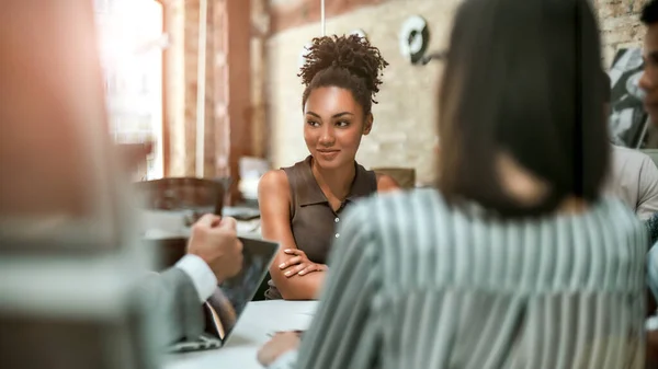 Rád tu pracuju. Mladá a veselá afro americká žena se usmívá a dívá se stranou při setkání s kolegy v moderní kanceláři — Stock fotografie