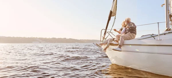 Rüyaları keşfet. Sakin bir mavi denizde yelkenli teknenin yanında oturan mutlu bir çift. Manzaranın keyfini çıkarırken kadınına sarılan adam.