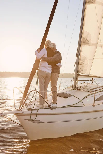 Sadece biz varız. Denizde yüzen yelkenli ya da yat güvertesinde duran mutlu yaşlı çift. Erkek ve kadın birbirlerine sarılıyorlar, manzaranın tadını çıkarıyorlar. — Stok fotoğraf