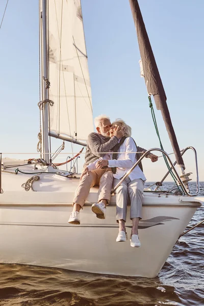 快乐的老夫妇坐在船舷或游艇甲板上漂浮在海面上。男人亲吻女人，欣赏风景 — 图库照片