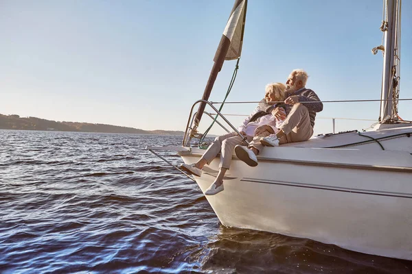 Yelkenciliğe âşığım. Sakin bir mavi denizde yelkenli teknenin yanında oturan mutlu bir çift. Manzaranın keyfini çıkarırken kadınına sarılan adam. — Stok fotoğraf