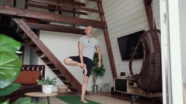 Pose de árvore. Atlético maduro homem exercitando em casa, fazendo ioga, praticando diferentes asanas de ioga — Vídeo de Stock