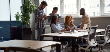 Birlikte çalışma alanında başarılı bir proje ekibi. Modern ofiste birlikte çalışan genç çok kültürlü iş adamları dizüstü bilgisayar, tablet ve akıllı telefon kullanıyorlar.