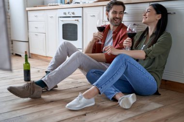 Yıldönümünü kutluyoruz. Modern mutfakta yerde oturmuş kırmızı şarap içen ve birlikte güzel vakit geçiren genç ve güzel bir çift.