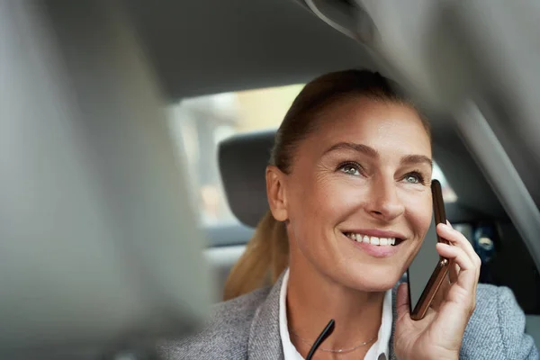 Miło się rozmawiało. Portret odnoszącej sukcesy atrakcyjnej bizneswoman rozmawiającej przez telefon komórkowy i uśmiechniętej siedzącej na tylnym siedzeniu w samochodzie — Zdjęcie stockowe