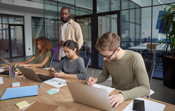 Erfolgreiche Geschäftsleute. Gruppe junger multiethnischer Menschen, Mitarbeiter, die im modernen Büro zusammenarbeiten, Laptops und Smartphones benutzen und Notizen machen — Stockfoto