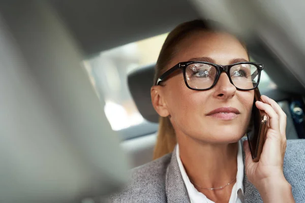 Biznesowa rozmowa. Portret odnoszącej sukcesy kobiety biznesu noszącej okulary rozmawiającej przez telefon komórkowy siedząc na tylnym siedzeniu w samochodzie — Zdjęcie stockowe