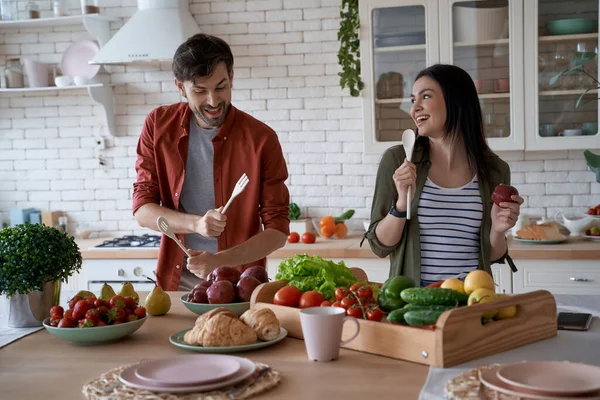 Feeling happy and carefree. Young playful family couple dancing, singing and having fun while preparing healthy food in the modern kitchen at home — Stock Photo, Image