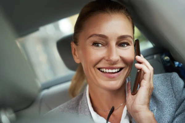 Zawsze dostępny. Portret pięknej i odnoszącej sukcesy kobiety biznesu rozmawiającej przez telefon komórkowy i uśmiechającej się siedząc na tylnym siedzeniu w samochodzie — Zdjęcie stockowe