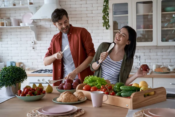 Enjoying cooking together. Young happy family couple, wife and husband having fun while preparing healthy food in the modern kitchen at home — Stock Photo, Image