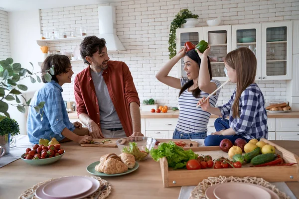 Çocuklarla güzel bir aile mutfakta yemek pişirirken eğleniyor. Anne, baba ve iki küçük çocuk salata hazırlayıp sebzelerle oynuyorlar. — Stok fotoğraf
