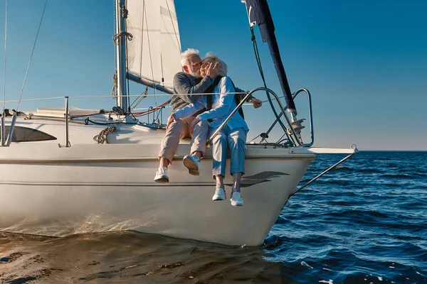 Romantic elderly couple embracing and kissing while relaxing on sail boat or yacht deck floating in a calm blue sea at sunset