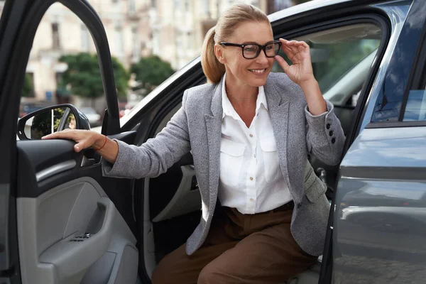 Portret pięknej i szczęśliwej biznesmenki w okularach wysiadającej z nowoczesnego samochodu i uśmiechniętej. Dotarcie do biura — Zdjęcie stockowe