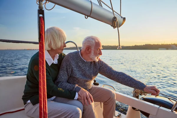 People lifestyle concept. Senior couple, elderly man and woman sitting on the sailboat or yacht deck floating in sea, sailing together on a sunny day