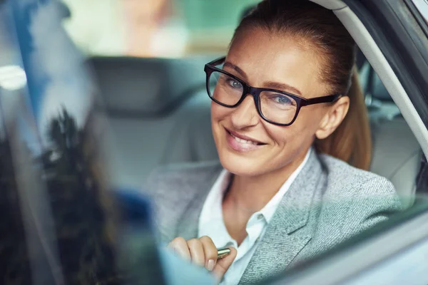 Biznesmenka w samochodzie. Wesoła kobieta w średnim wieku w okularach siedząca na tylnym siedzeniu taksówki, patrząca w kamerę i uśmiechnięta — Zdjęcie stockowe