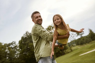 Mutlu bir baba ve küçük kızı sıcak bir yaz gününde parkta eğleniyorlar. Birlikte vakit geçirirken çok mutlu ve gülümsüyorlar.