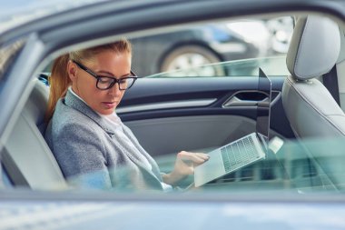 İş toplantısına giden yolda çalışıyorum. Arabada arka koltukta otururken dizüstü bilgisayar kullanan orta yaşlı bir iş kadınının yan görüntüsü.