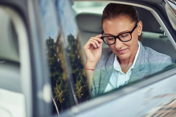 Beautiful middle aged business woman adjusting her eyeglasses while sitting on back seat in taxi