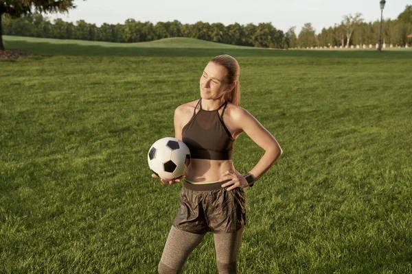 Fußball-Mädchen. Schöne sportliche junge Frau hält Fußball in der Hand und lächelt in die Kamera, während sie draußen auf einer grünen Wiese steht — Stockfoto