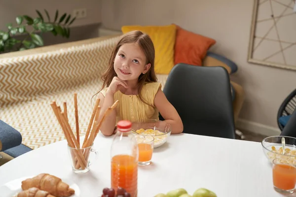 Retrato de linda y feliz niña caucásica sentada en la mesa de la cocina en casa y desayunando — Foto de Stock