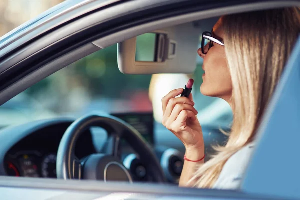 Doing make up in car, side view of a beautiful business woman sitting behind steering wheel and using lipstick Stock Image