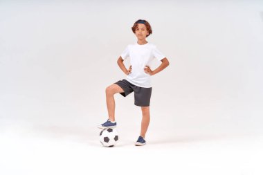 Futbolcu. Futbol topuyla mutlu bir gencin, gri arka planda izole bir şekilde kameraya bakıp gülümsediği uzun bir çekim.