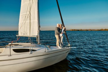 Tekne gezisi. Mutlu son sınıf öğrencisi erkek ve kadın, sakin mavi denizde birlikte yüzerken yelkenli ya da yat güvertesinde durup harika manzaranın tadını çıkarıyorlar.