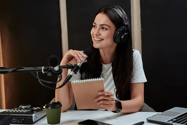 Portait de atractiva joven presentadora de radio sonriendo a un lado mientras habla en micrófono, moderando un espectáculo en vivo —  Fotos de Stock