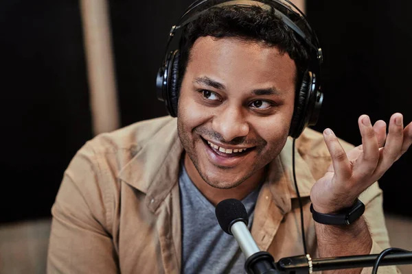 Close up of happy young male radio host smiling aside while broadcasting in studio, using microphone and headphones — Stock Photo, Image