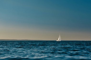 Gün batımında denizde yüzen beyaz yelkenli yelkenli ya da yat. Görkemli manzara, huzur ve sükunet.