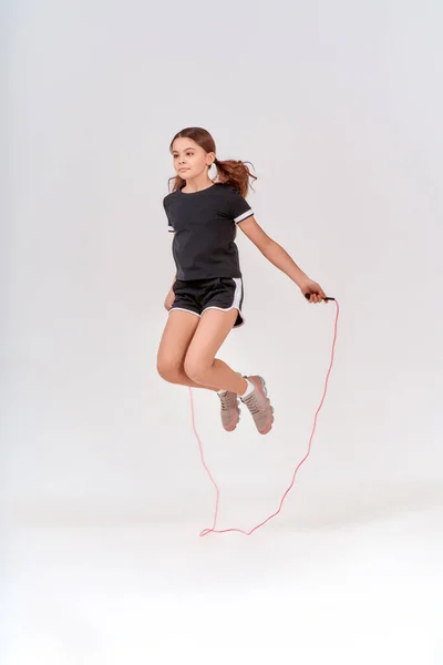 Saludable y activo. De cuerpo entero de una linda adolescente saltando con una cuerda de salto aislado sobre fondo gris en el estudio — Foto de Stock