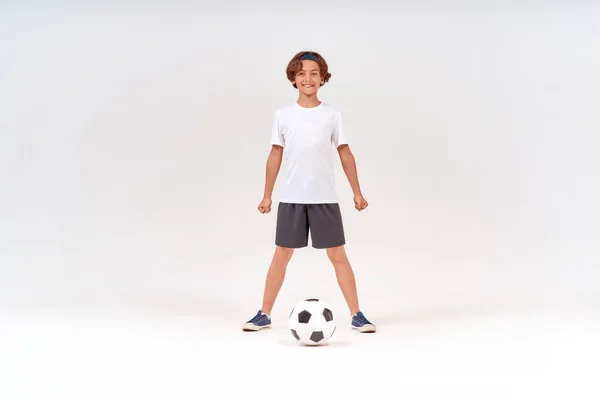 Futbol oynayan, kameraya bakıp gülümseyen, gri arka planda tek başına duran mutlu bir gencin tam boy görüntüsü. — Stok fotoğraf